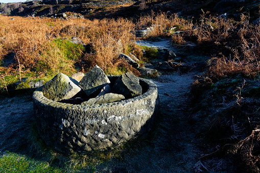 An abandoned cylindrical carved gritstone object stands close to frost covered footpaths on the slopes of Burbage Edge.