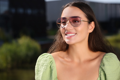 Beautiful smiling woman in sunglasses outdoors, space for text