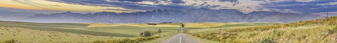 Panoramic image of a paved, empty road running straight towards a mountain range on the horizon during daytime
