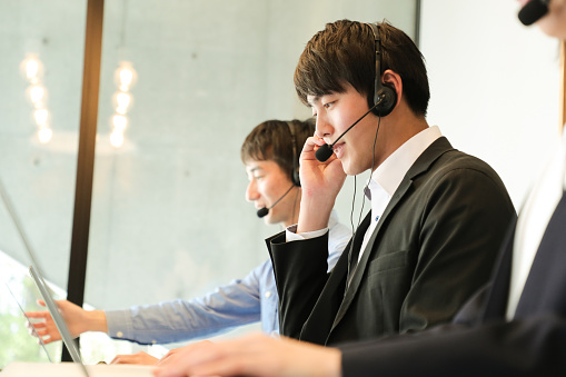 Customer service agents with headsets assisting customers over the phone.\nMale Customer service representatives helping to support their customers in modern office locations.