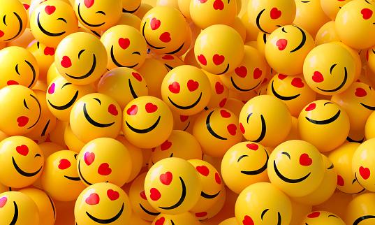 Yellow spheres textured with happy face emoji on yellow background. Horizontal composition.