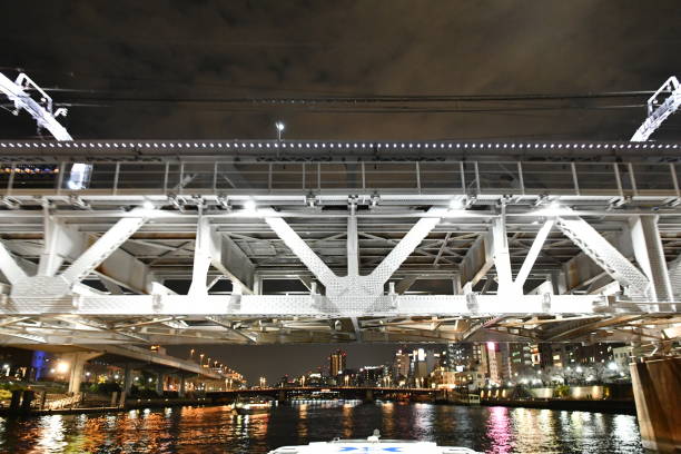 An idyllic scene of a small white boat sailing peacefully underneath a large bridge structure