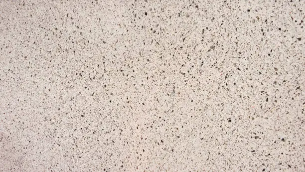 Photo of texture of grainy quartz in beige sand color, closeup view. light white marble stone texture with splashes and marble chips. terrazzo background for furnishing furniture.