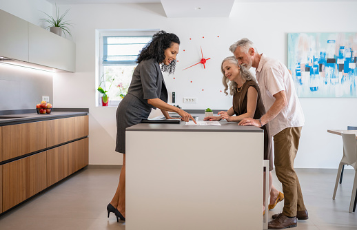 Couple and female real estate agent checking property for sale brochure while standing near kitchen counter. Luxury lifestyle and new beginning concept.