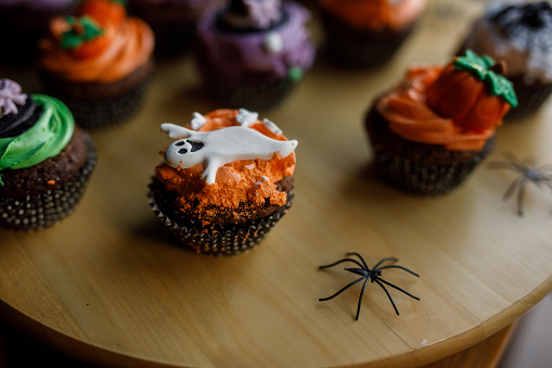 Close up shot of various adorable Halloween themed cupcakes served on a wooden plate.
