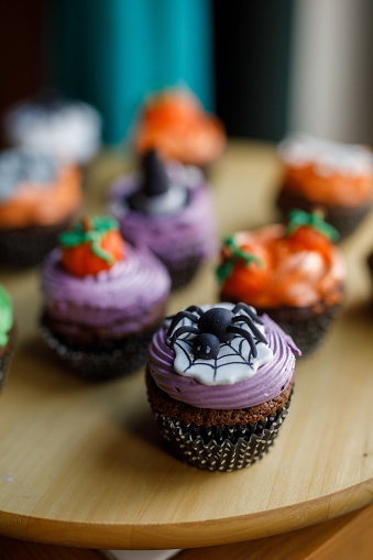 Close up shot of various adorable Halloween themed cupcakes served on a wooden plate.