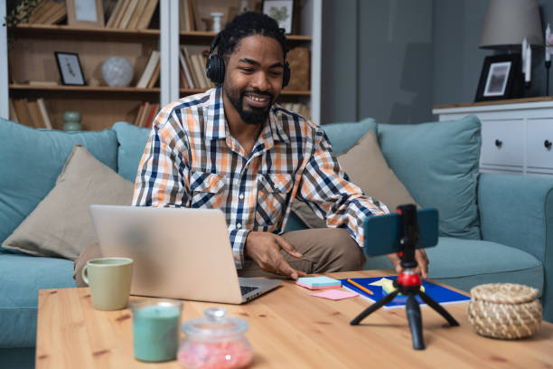 istock Happy millennial African American man in headset having web call using laptop computer and smartphone sitting on couch talking at webcam in home office. Video conference online business meeting. 1922530992
