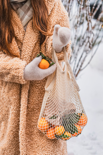 Cotton mesh bag with fresh colorful citrus fruits in hands of girl. Eco friendly, zero waste, shopping and healthy lifestyle concept