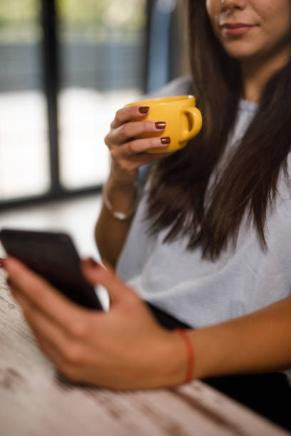 istock Young woman sipping coffee and checking text messages on smart phone 1922562232