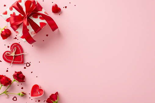 Delight in magic of giving with Valentine's Day ensemble. Top view reveals gift box, red roses, and heart-shaped confetti on pastel pink settingâ€” perfect tableau for your heartfelt sentiments