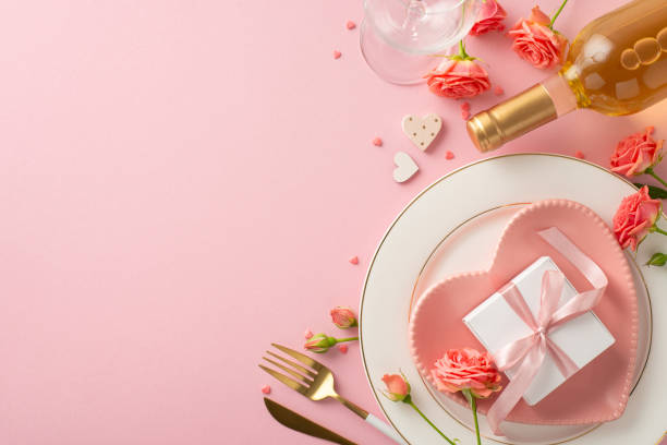 istock Romantic Dining Experience: Top view photo of exquisite table setting featuring heart-shaped plate, cutlery, white wine, roses, sprinkles on pastel pink background. Ample space for text or advertising 1922567111