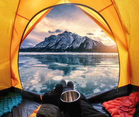 View from inside a tent of tourist relaxing and looking to the rocky mountains with bubbles frost on Abraham Lake in winter at Alberta, Canada