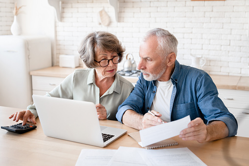 Busy caucasian old elderly senior couple making calculations at home kitchen, checking the document, revising data, information, counting domestic bills and rentals