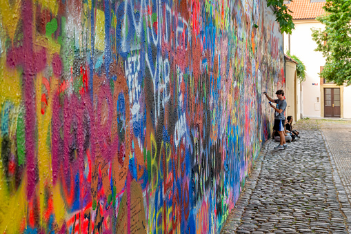 Prague, Czech Republic - July 7, 2016: People filling the Lennon Wall; located in a secluded square across from the French Embassy, the wall had been decorated by love poems and short messages.