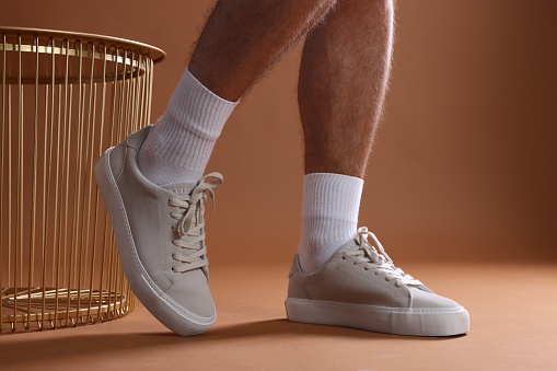 Man wearing stylish sneakers on brown background, closeup