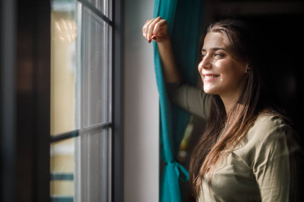 istock Young woman standing by the window, looking outside 1922644289
