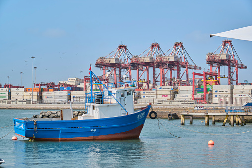 Small fishing boat near dock and containers in the port of Callao.