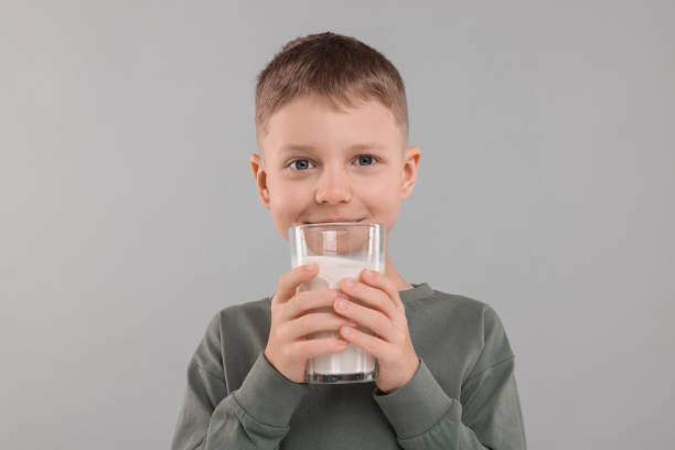 istock Cute boy with glass of fresh milk on light grey background 1922656413