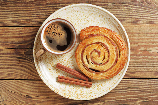 Cup of coffee and cinnamon roll on a plate on wooden background, top view