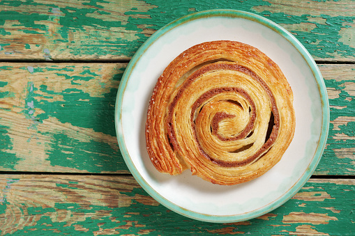 Cinnamon roll on a plate on old green wooden surface, top view with copy space