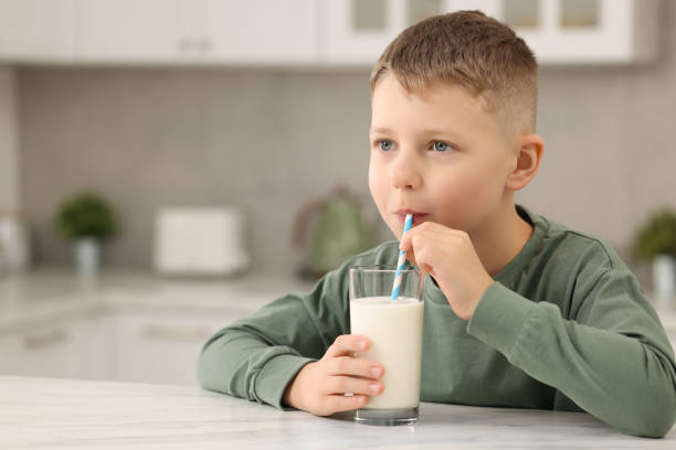 istock Cute boy drinking fresh milk from glass at white table in kitchen, space for text 1922660644