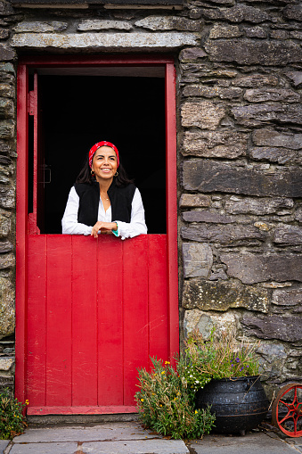 Young woman photographed while leaning on a red door of a beautiful and unique house in rural Ireland