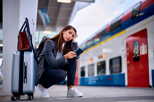 Young thoughtful woman using cell phone while waiting at train station. Copy space.