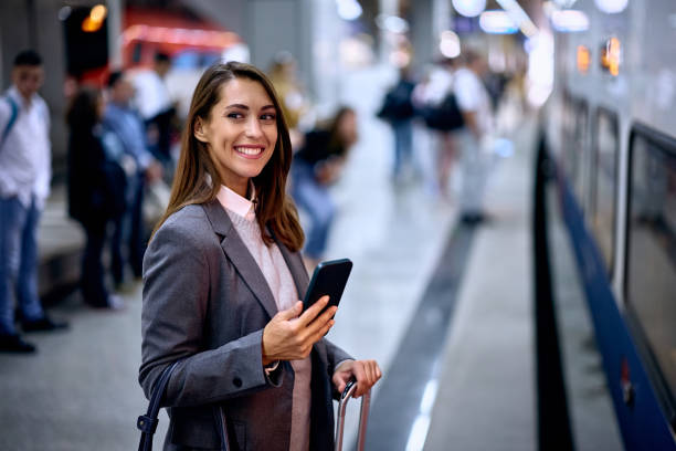 istock Young happy woman using cell phone while waiting for a train at the station. 1922705987