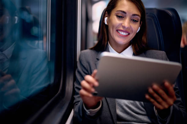 istock Happy businesswoman using earbuds and touchpad while commuting by train. 1922706142