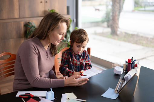 Child boy and mother doing origami toys using colored papers by following the steps instructed in the video tutorial on digital tablet