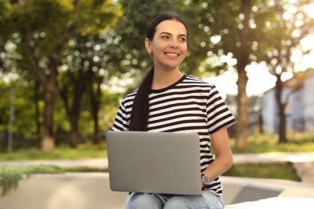 istock Happy young woman using modern laptop outdoors 1922733618