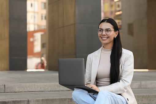 Happy young woman using modern laptop outdoors. Space for text