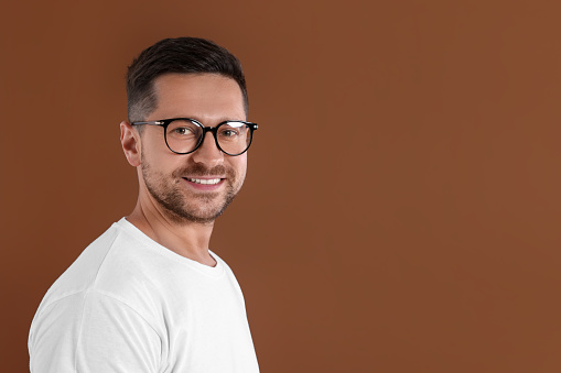 Portrait of happy man in stylish glasses on brown background. Space for text