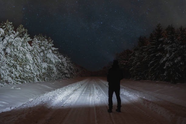 istock Winter night scene, a man with a flashlight in a snowy forest on the road, starry sky with clouds. 1922789836