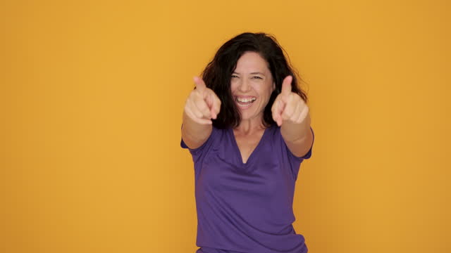 The young woman is jumping for joy while looking at the camera against an orange background.