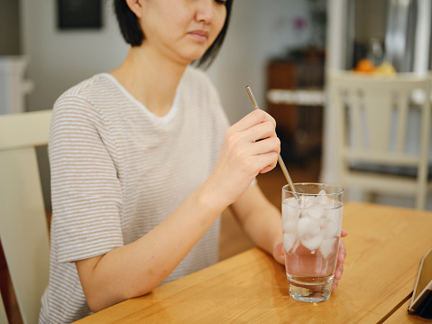 An Asian woman in a home kitchen experiencing tooth pain.