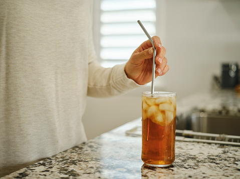 A close up of a woman’s hands putting a reusable metal straw in an iced drink in a home kitchen.