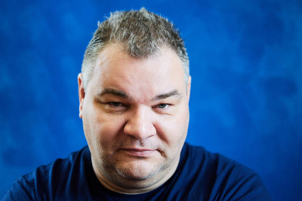 istock Looking from under his brows, Caucasian man, 47 years old, stares with his head slightly lowered, his face close-up on blue background. 1922830017
