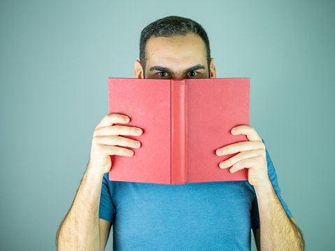 Young man hiding part of his face with red cover book Looking at camera