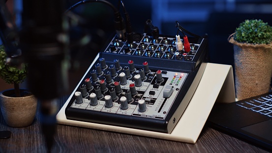 Panning shot of professional analog mixer and microphone used to produce high fidelity audio during podcast recording session in studio. High tech recording devices on table in apartment