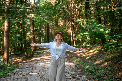 Adult woman with long blond hair and a straw hat, wearing light summer clothes, enjoying summertime in the woods.