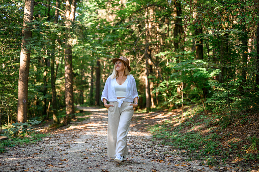 Adult woman with long blond hair and a straw hat, wearing light summer clothes, enjoying summertime in the woods.