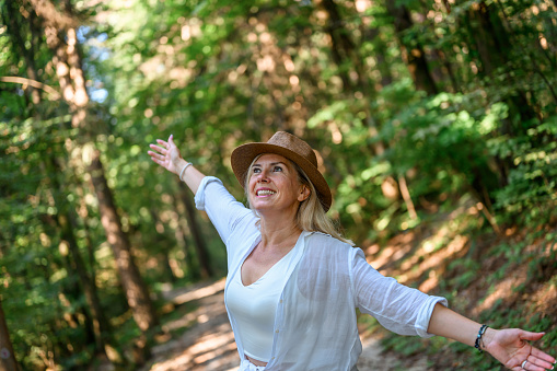 Adult woman with long blond hair and a straw hat, wearing light summer clothes, enjoying summertime in the woods.