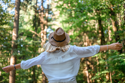 Rear view of an adult woman with long blond hair and a straw hat, wearing light summer clothes, enjoying summertime in the woods.