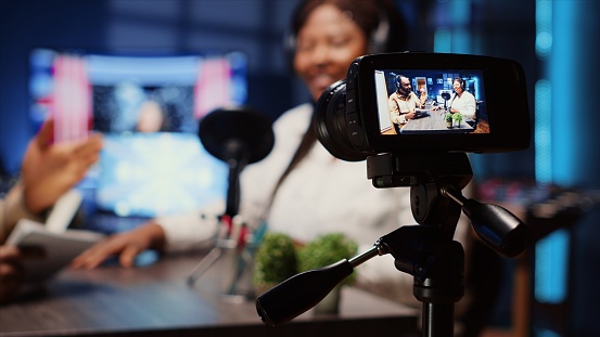 Focus on professional camera recording man in blurry background using high tech microphones to interview guest, ensuring optimum video and sound quality for audience watching at home, close up