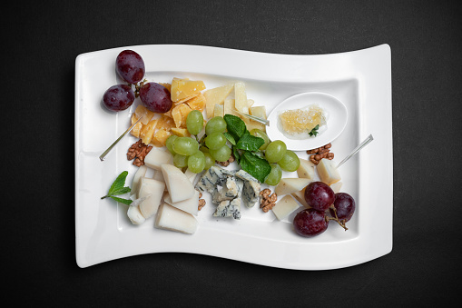 close up of cheese platter with grape and nuts on dark background