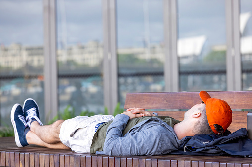 Sydney, Australia _ January 07, 2024: Tired young man sleeping on public bench at Circular Quay