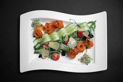 fresh salad with arugula, tomatoes, cucumber and salted salmon on white plate