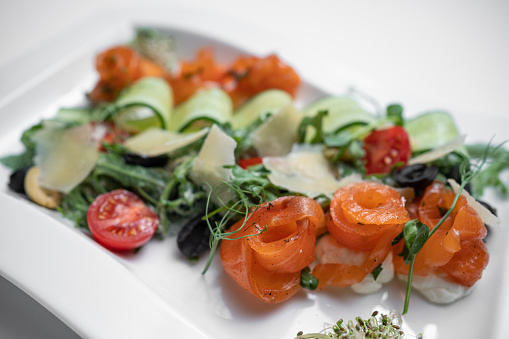 fresh salad with arugula, tomatoes, cucumber and salted salmon on white plate