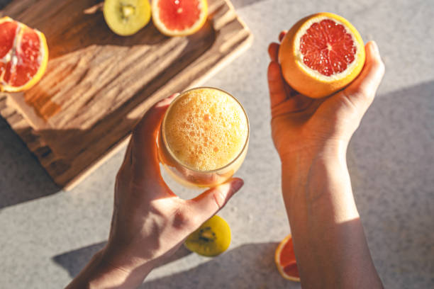 istock Woman hand with juice glass and oranges on kitchen table background., top view. 1922943821